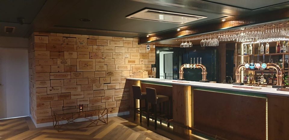The bar at The Bank, with a copper counter, hanging stemware and a wall built from wooden wine-case panels