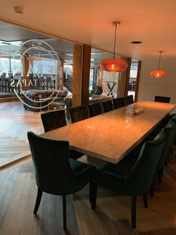 The private dining room: a long marble table with green velvet chairs under copper pendant lights, behind glass etched with the venue's roundel